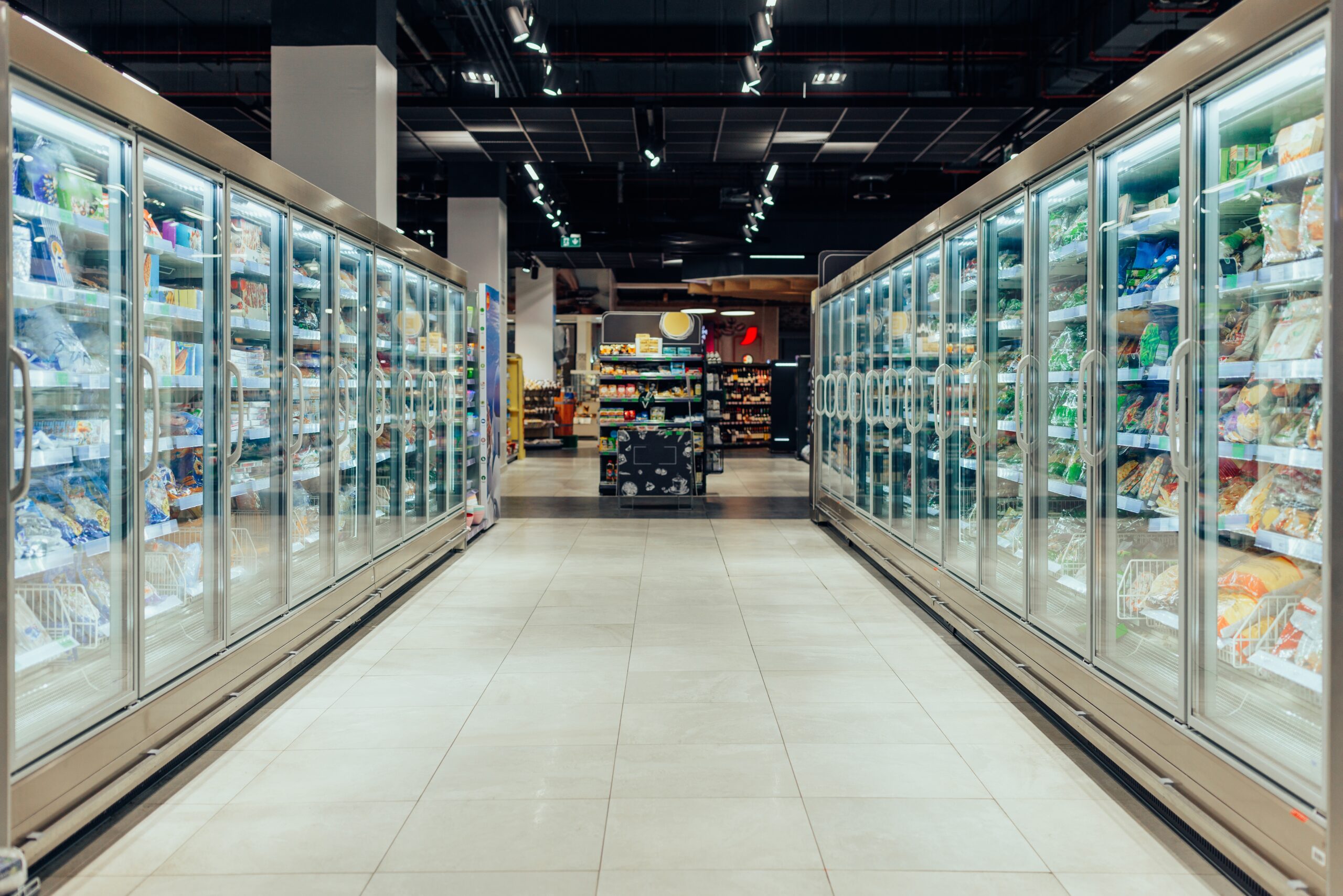 Aisle with refrigerated shelves filled with various products in a well-lit grocery store.
